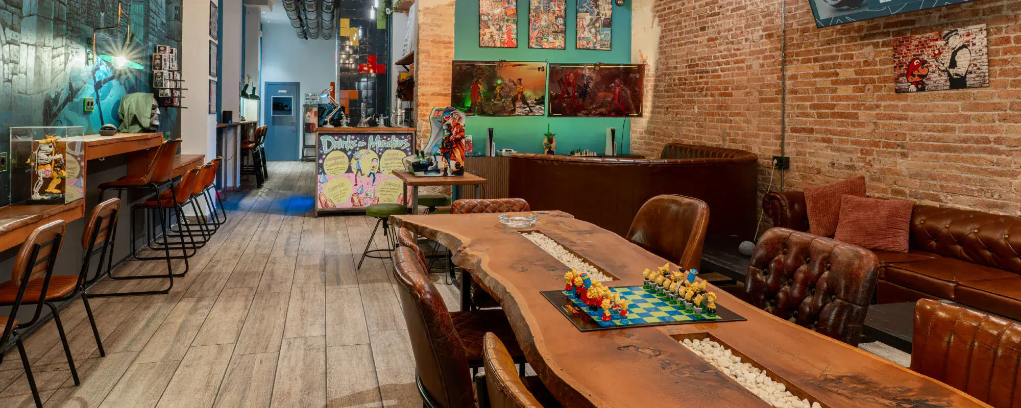 Modern interior of 1UP Social Club in Barcelona with wooden communal table, leather seating, gaming setup, and exposed brick walls.