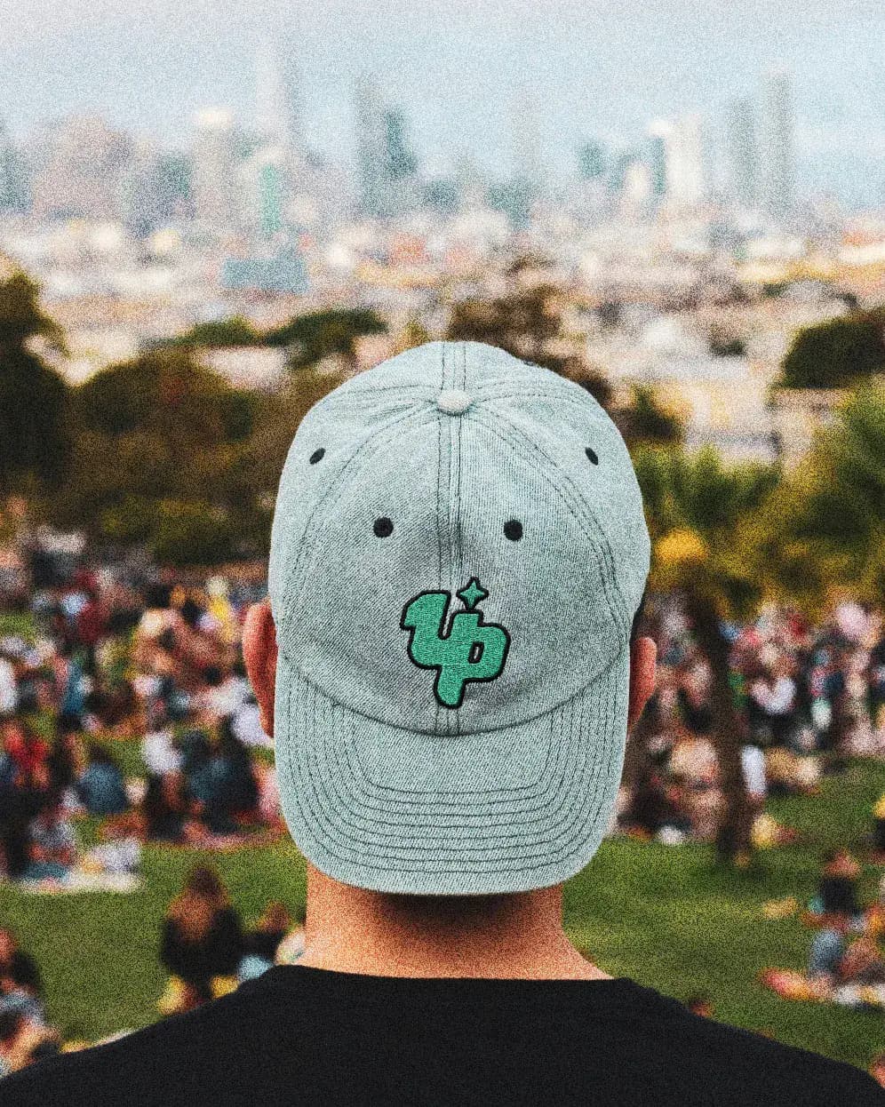 Person wearing grey cap embroidered with ONEUP logo overlooking Barcelona city skyline.